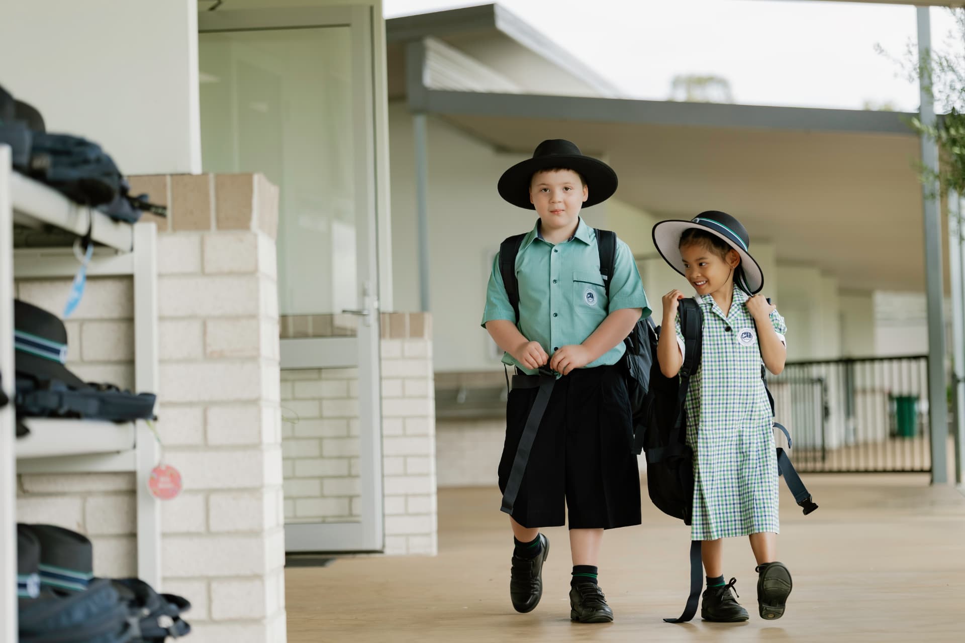Two Border Rivers primary students walking along a covered College walkway with their bags and hats