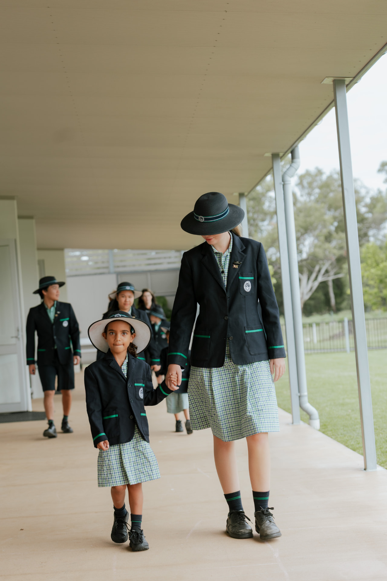 A senior Border Rivers student walking hand in hand with a Prep student along a College verandah